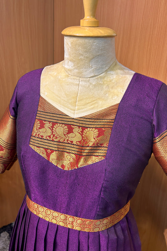 The rich purple silk fabric is accentuated with golden zari borders on the sleeves and hem, adding a luxurious ethnic charm. The pleated skirt enhances the flow and fall of the gown, while the fitted waist yoke offers a flattering silhouette. A perfect choice for women who love traditional attire with a designer twist.

Key Features:

💜 Color: Royal Purple with Gold Zari Accents

🧵 Fabric: Premium Silk Blend with lining

✂️ Design: Fitted Waist Yoke | Knife Pleats | Elbow Sleeves